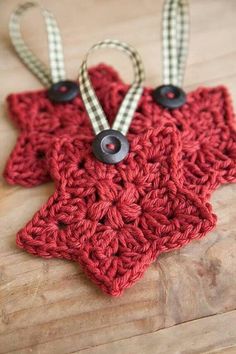 two crocheted star ornaments with black buttons on them sitting on a wooden surface