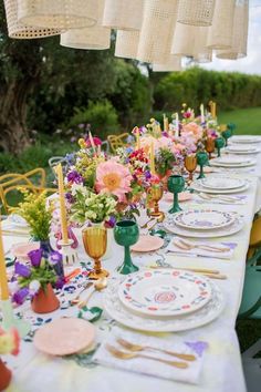 a long table is set with plates and candles for an outdoor dinner party in the garden