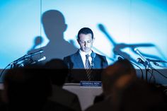 a man in a suit and tie standing at a podium with microphones behind him