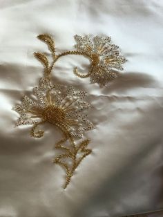 two embroidered flowers on a white satin sheet with gold threadwork and bead work