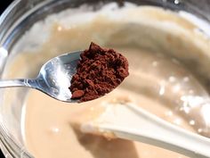 a spoon filled with chocolate and powder on top of a glass bowl full of milk