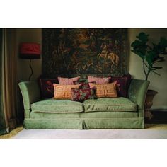 a green couch with pillows on it in front of a tapestry wall hanging above the couch