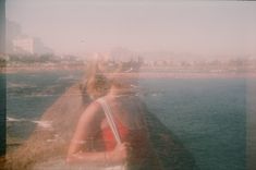 two people standing on top of a cliff next to the ocean with buildings in the background