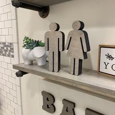 two wooden figures on top of a shelf above a bath room sink with a sign that says you