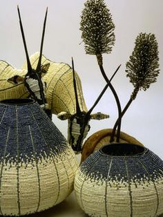 two vases with plants in them sitting on a table next to each other and one is made out of woven material