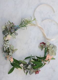 a wreath made out of flowers and greenery on a marble surface with a white ribbon