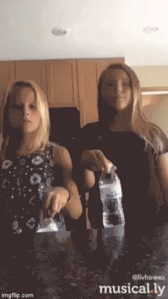 two women standing in front of a kitchen counter with water bottles on top of it