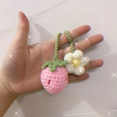 a hand is holding a tiny crocheted strawberry and flower brooch on it's thumb