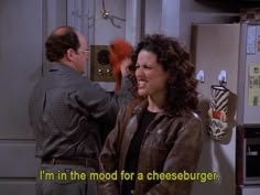 a woman standing next to a man in a kitchen talking on a cell phone with the caption i'm in the mood for a cheeseburger