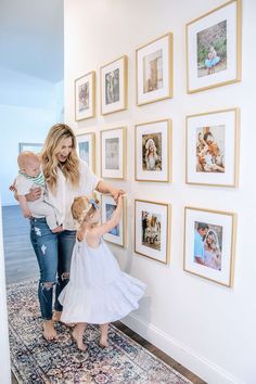 a woman and two children are looking at pictures on the wall in front of them