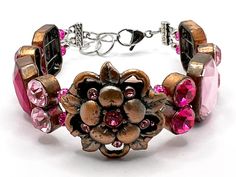 This large double-strand bracelet has rhinestone beads in various shades of pink with pink crystal spacers. There is a large copper toned flower which acts as the centerpiece for this bracelet. It is strung on high quality bead stringing wire with a lobster claw clasp and is adjustable from 7-1/2 to 8-1/2 inches (M/L). Bead Stringing, Rhinestone Bead, Strand Bracelet, Rhinestone Bracelet, Pink Rhinestones, Shades Of Pink, Pink Crystal, Lobster Claw, Patina