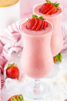 two glasses filled with strawberry milkshakes sitting on top of a table next to strawberries