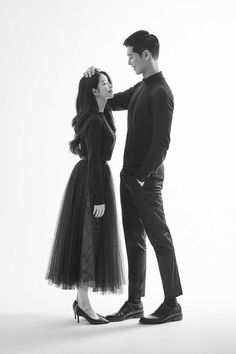 a man standing next to a woman in a black dress and high heeled shoes