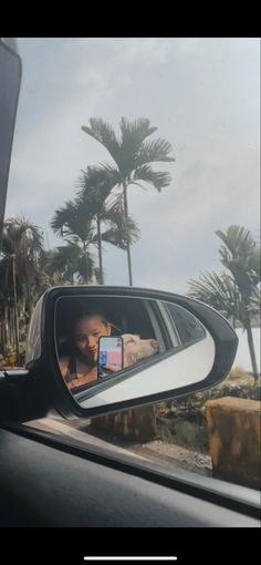 a person taking a photo in the side mirror of a car with palm trees behind them