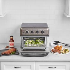 a toaster oven with food cooking in it on a counter top next to white cabinets