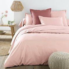 a bed with pink sheets and pillows in a room next to a rug on the floor