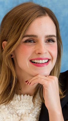 a close up of a person wearing a suit and smiling at the camera with her hand on her chin