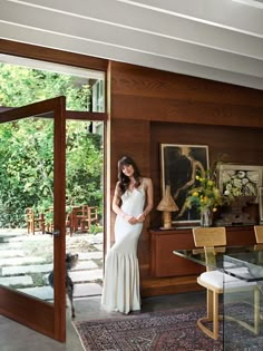 a woman in a white dress standing next to a glass table with flowers on it