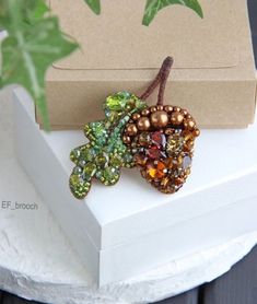 two brooches sitting on top of a table next to a box with leaves