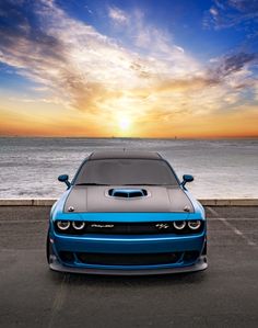 a blue car is parked in front of the ocean at sunset or sunrise with clouds