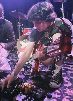 two young men are playing guitars on the floor