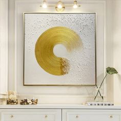 a white dresser with a gold circle painting on the wall above it and a potted plant next to it