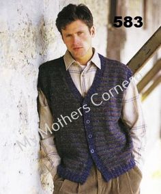 a man leaning against a wall wearing a sweater vest