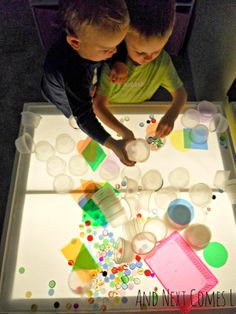 two young boys standing at a table with an interactive light box on the bottom floor