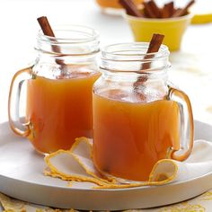 two mugs filled with liquid sitting on top of a white plate next to cinnamon sticks