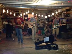 a group of people playing guitars in a room with lights strung from the ceiling and music equipment