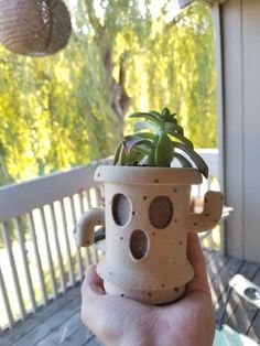 a person holding up a potted plant with holes in it's middle on a porch