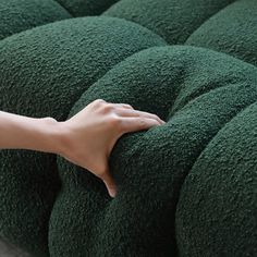 a person's hand on the back of a green cushion that is folded over