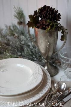 a table set for christmas with silverware and pine cones in a vase on top