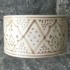 a white and brown vase sitting on top of a stone floor next to a wall