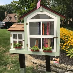 a book shelf with flowers and books on it in front of a flower garden area