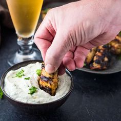 a person dipping some food into a bowl with ranch dressing on the side and a glass of beer in the background