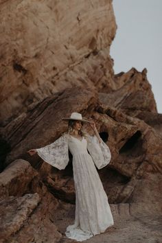 a woman in a white dress and hat standing on rocks