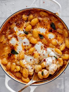 a pot filled with pasta and cheese on top of a table next to a spoon