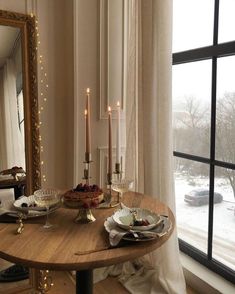 a wooden table with plates and candles on it in front of a large window that has snow outside