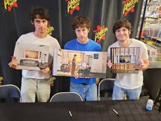 three young men holding up pictures in front of a table