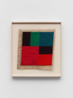 an abstract painting with red, green and black squares in a white frame on the wall