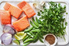 raw salmon, green beans, onions and herbs on a cutting board with seasoning