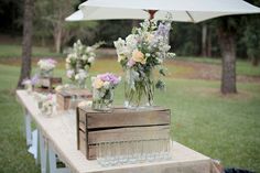 a table with vases filled with flowers and glasses on top of it next to an umbrella