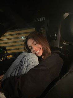 a woman sitting in the passenger seat of a car smiling and looking at the camera