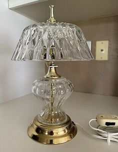 a glass table lamp sitting on top of a white counter next to a charger