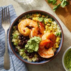 a bowl filled with shrimp, black beans and guacamole next to a fork