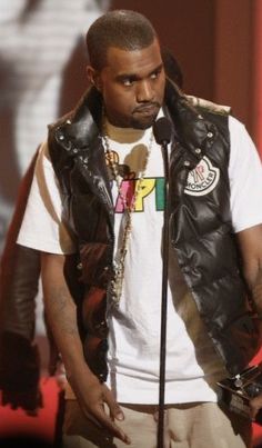 a man standing in front of a microphone wearing a black vest and white t - shirt