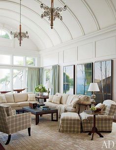 a living room with couches, chairs and lamps on the ceiling in front of large windows