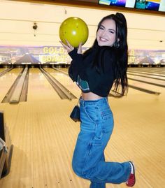 a woman holding a green bowling ball in her right hand and smiling at the camera