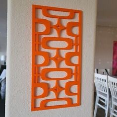 an orange wall hanging on the side of a white wall next to a dining room table